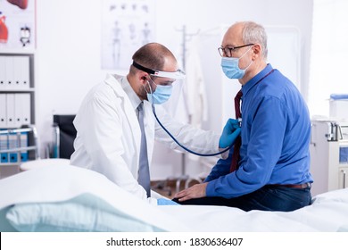 Doctor listening heart beat of senior man with stethoscope during examination on hospital room to give a diagnosis and using protection mask for covid-19. - Shutterstock ID 1830636407