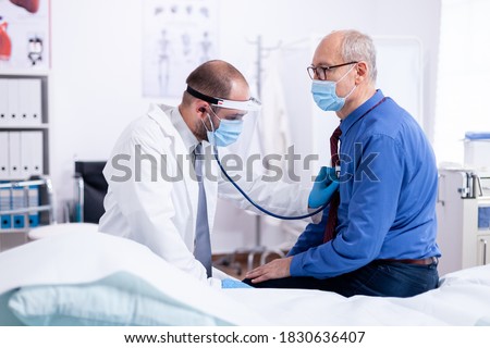 Doctor listening heart beat of senior man with stethoscope during examination on hospital room to give a diagnosis and using protection mask for covid-19.