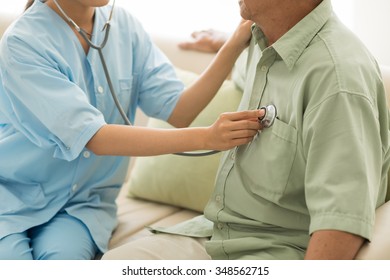 Doctor Listening To Heartbeat Of Senior Patient At Home