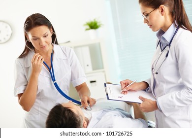 Doctor listening to the patientÃ?Â¢??s internals using stethoscope, nurse taking notes