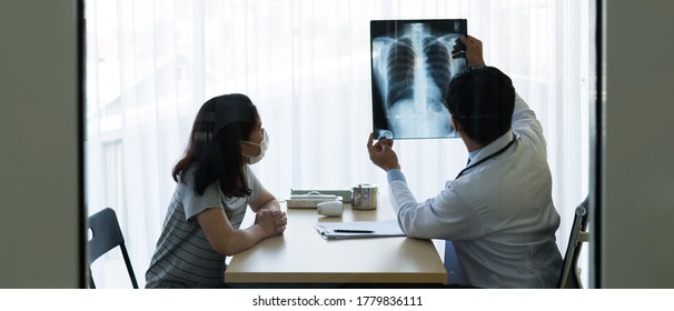 Doctor Looking At Chest X-ray Of The Asian Woman Patient Who Come And Visit At Outpatient Clinic In The Hospital (view Via Window). Healthcare And Medical Concept