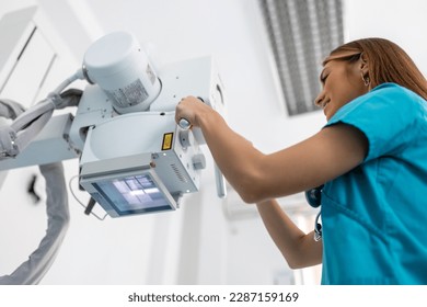Doctor looking at X-ray machine in clinic. Female doctor sets up the machine to x-ray over patient. Radiologist and patient in a x-ray room.