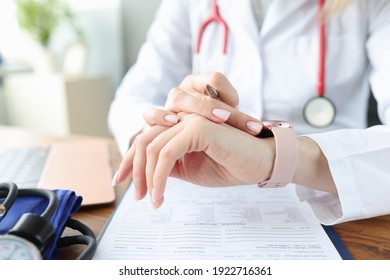 Doctor Looks At Clock At Work Table In Medical Office. Irregular Working Hours For Health Workers Concept