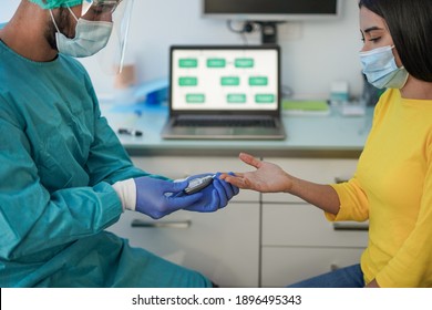 Doctor Making Blood Sugar Test To A Young Woman In Medical Clinic For Diabetes - Medical Worker And Patient Wearing Surgical Face Masks For Coronavirus