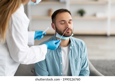 Doctor making covid-19 PCR test for male patient at home. Millennial guy undergoing coronavirus diagnostic procedure indoors. Viral disease prevention and treatment concept - Shutterstock ID 1990126760