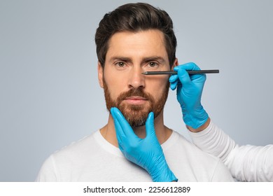 Doctor making marks on male patient's face, middle aged man on consultation at surgeon, standing on grey background. Facial plastic surgery concept - Powered by Shutterstock