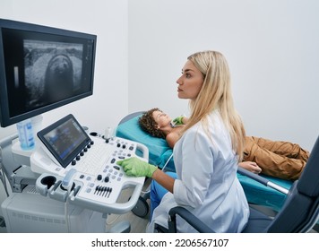 Doctor Making Ultrasonography To Male Child Patient At Ultrasound Office Of Medical Clinic. Ultrasound Diagnostics Of Thyroid Gland For Children