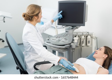 Doctor Making Ultrasound Scan Of Stomach To Smiling Patient And Pointing At Blank Screen