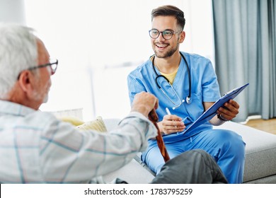 Doctor Or Male Caregiver With Senior Man Holding A Cane On Sofa At Home Or Nursing Home