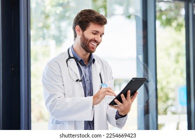 Doctor, man and tablet for research at hospital for social media app, email and networking by window. Happy medic, communication or typing medical advice for help, consulting or chat on web at clinic - Powered by Shutterstock