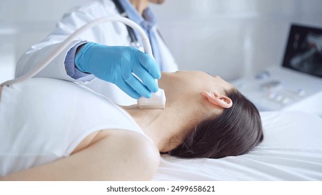 Doctor man wearing blue medical gloves is using ultrasound equipment on neck of female patient lying down for a medical examination - Powered by Shutterstock