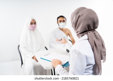 Doctor In A Mask Asks The Husband And Wife Of Prospective Hajj Pilgrims During A Health Consultation In The Room