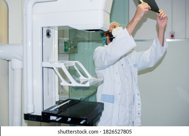 Doctor With Mask Checking Mammography Of Woman In X-ray Room.