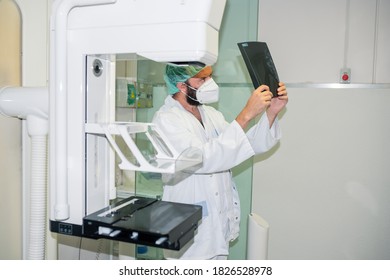 Doctor With Mask Checking Mammography Of Woman In X-ray Room.