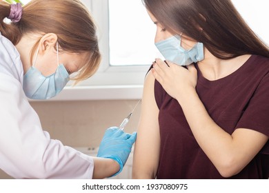 Doctor in mask giving an injection of a vaccine to a teenager girl in a medical clinic, vaccine prevention against infection with coronavirus