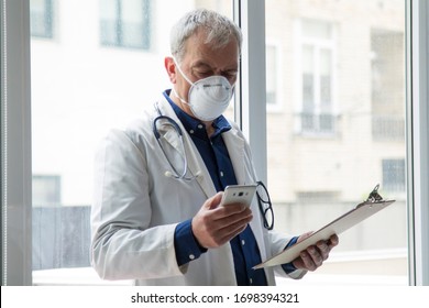 Doctor With Mask Using Mobile Phone And Reading Clinical Reports