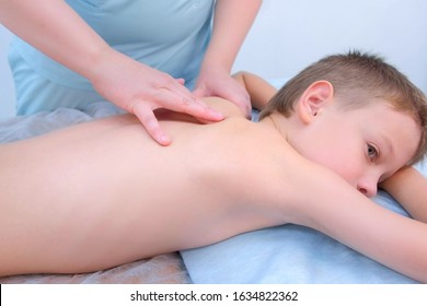 Doctor Massagist Making Therapeutic Massage To Teen Boy On Spine In Clinic, Side View. Child Boy Is Lying On Couch And Talking. Rehabilitation Massage After Injury. Medicine And Treatment To Children.