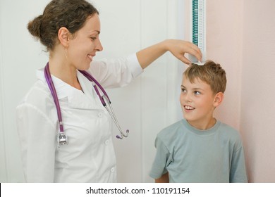 Doctor measures growth smiling boy in medical office, focus on doctor