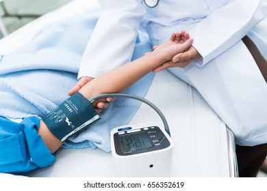Doctor measuring blood pressure on a girl lying on a hospital bed with Digital Sphygmomanometer. Doctor's hand holding the child patient. - Shutterstock ID 656352619