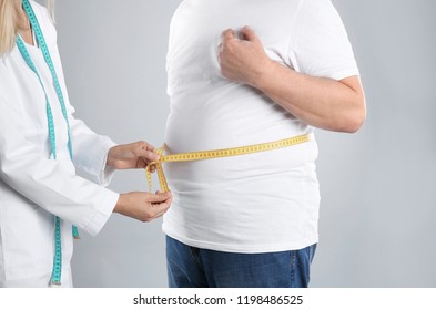 Doctor measuring senior man's waist on grey background. Weight loss - Powered by Shutterstock