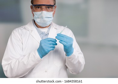 Doctor With Medical Face Mask And Medical Gloves Holding A Syringe In Front Of A Clinic Room 