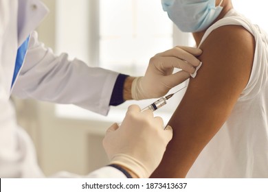 Doctor in medical gloves giving Covid-19, AIDS or flu antivirus vaccine shot to African-American patient. Close-up of hands holding syringe and cleaning skin on upper arm before antiviral injection