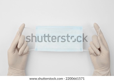 Doctor in medical gloves holding protective mask on white background, closeup