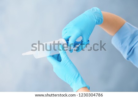 Doctor in medical gloves with large syringe on color background