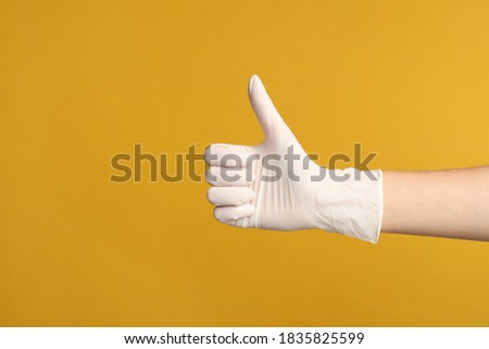 Doctor in medical gloves showing thumb up on yellow background, closeup. Space for text