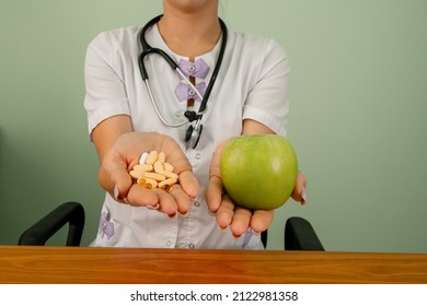 Doctor in medical gown offering alternatives fresh apple or pharmaceutical pills. Doctor holding apple or dietary food supplement pills. Health, choice between natural product and synthetic medicine.