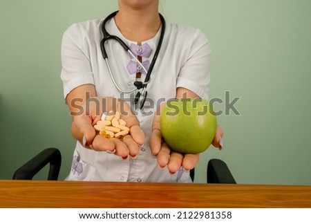 Doctor in medical gown offering alternatives fresh apple or pharmaceutical pills. Doctor holding apple or dietary food supplement pills. Health, choice between natural product and synthetic medicine.