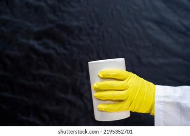 A Doctor In A Medical Gown And Protective Gloves Holds In His Hand A Large White Container Without Inscriptions. The Face Is Not Visible. Empty Template For Text.