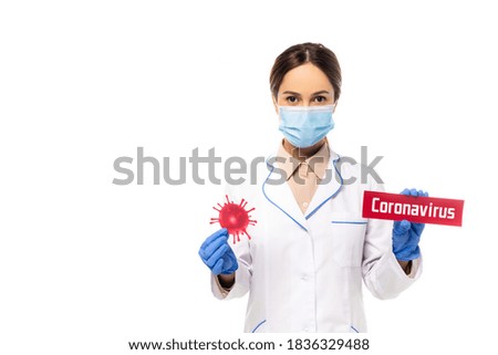 Doctor in medical mask holding bacteria and card with coronavirus lettering isolated on white