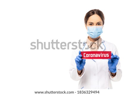 Doctor in medical mask holding card with coronavirus lettering isolated on white