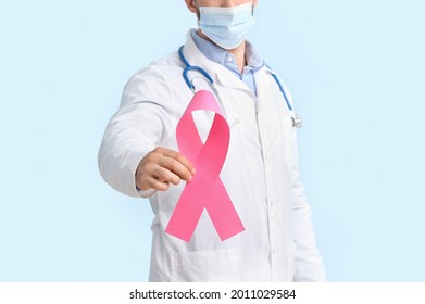 Doctor In Medical Mask And With Pink Ribbon On Color Background. Breast Cancer Awareness Concept