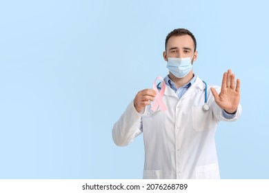 Doctor In Medical Mask And With Pink Ribbon On Color Background. Breast Cancer Awareness Concept