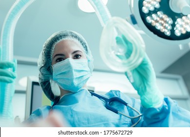 Doctor in medical mask and protective clothes standing with an anesthesia mask in her hand