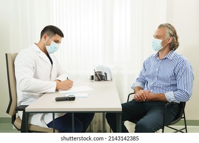 Doctor And Middle Aged Male Patient Wearing Prevention Masks During Consultation In Office