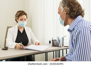 Doctor And Middle Aged Male Patient Wearing Prevention Masks During Consultation In Office