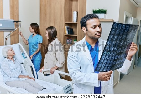 Doctor neurologist looking at MRI images of senior patient's head who is lying in ward of neurology department of hospital. Neurology and MRI of brain