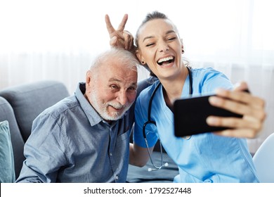 Doctor Or Nurse Caregiver Helping Senior Man With A Mobile Phone Taking Selfie At Home Or Nursing Home