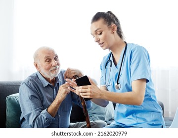 Doctor Or Nurse Caregiver Helping Senior Man With A Mobile Phone At Home Or Nursing Home