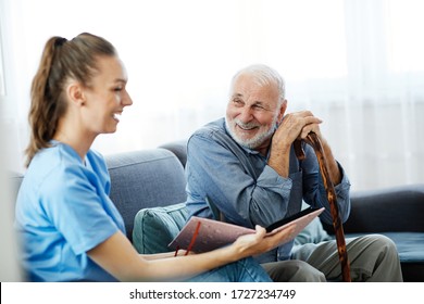 Doctor Or Nurse Caregiver With Senior Man Looking At Photo Album And Picture  At Home Or Nursing Home