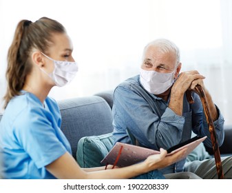 Doctor or nurse caregiver with senior man wearing protective masks looking at photo album and picture  at home or nursing home - Powered by Shutterstock