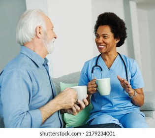 Doctor Or Nurse Caregiver With Senior Man Drinking Tea Or Coffee At Home Or Nursing Home