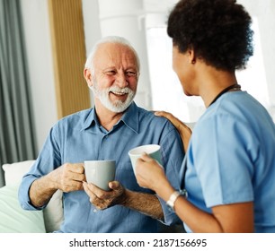 Doctor Or Nurse Caregiver With Senior Man Drinking Tea Or Coffee At Home Or Nursing Home