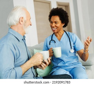 Doctor Or Nurse Caregiver With Senior Man Drinking Tea Or Coffee At Home Or Nursing Home