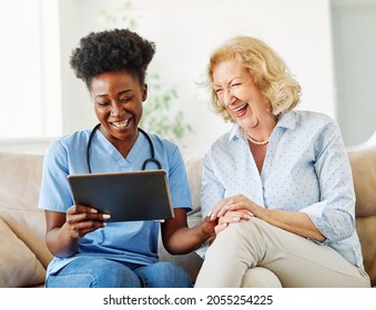Doctor or nurse caregiver showing a tablet screen to  senior woman and laughing at home or nursing home