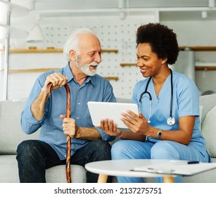 Doctor or nurse caregiver showing a tablet screen to  senior man and laughing at home or nursing home