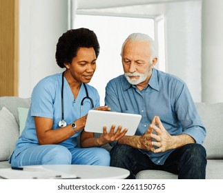 Doctor or nurse caregiver showing a tablet screen to  senior man and laughing at home or nursing home - Powered by Shutterstock